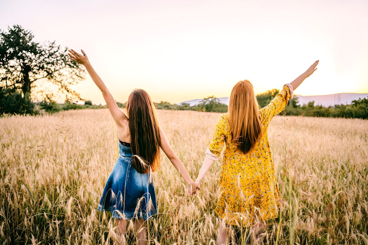 two women holding hands in field of wheat